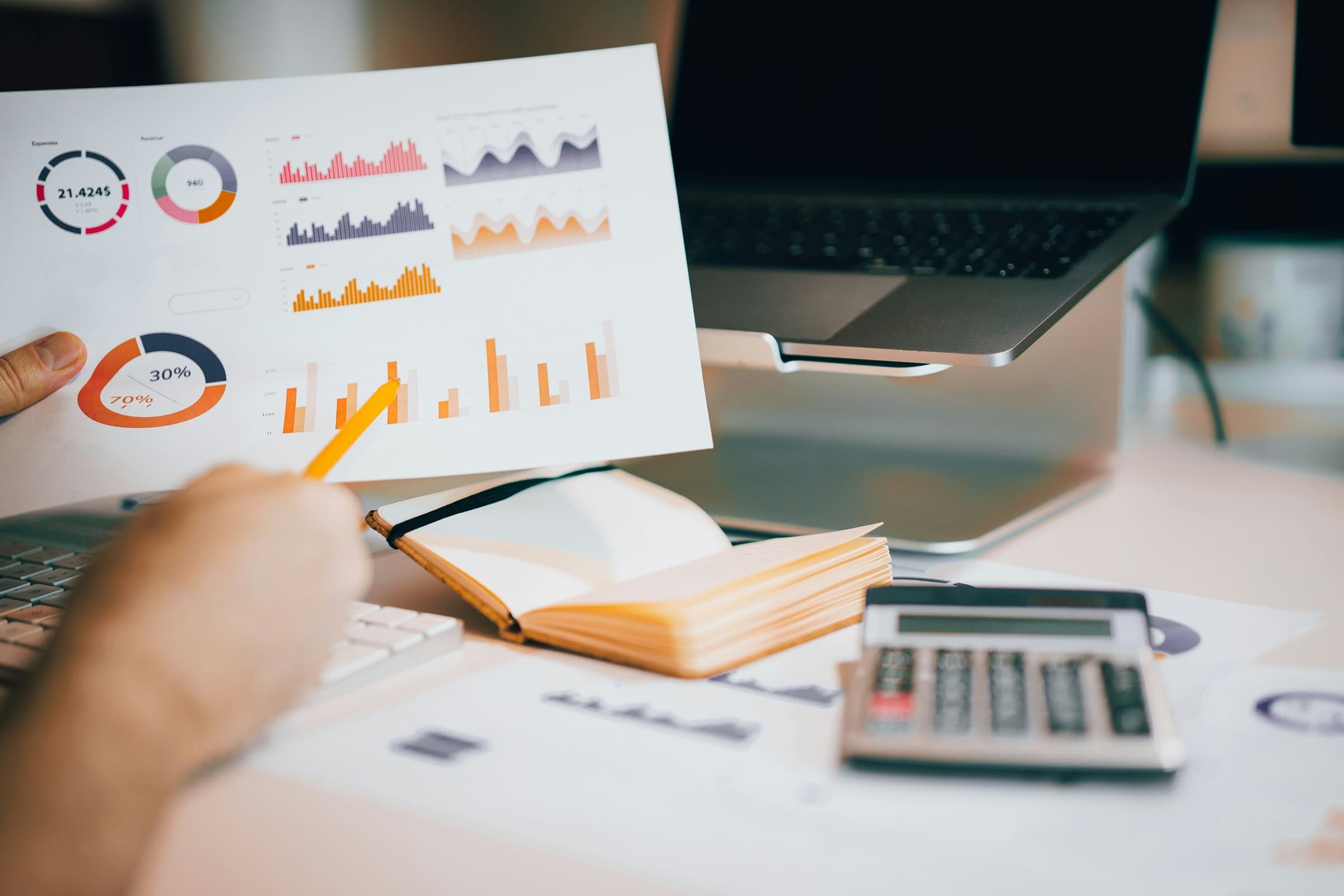 A hand holding up a printed sheet of scored charts, a pencil pointing at one of the bars
