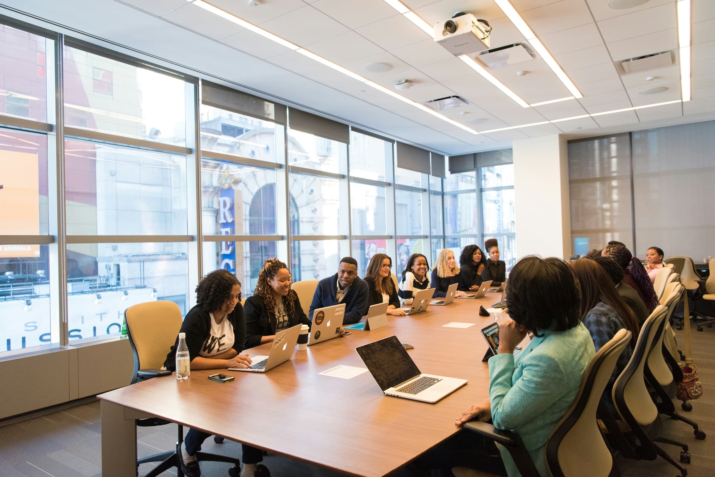 A long boardroom table lined with people at laptops, mid-meeting